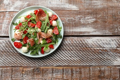 Photo of Tasty salad with arugula, mozzarella cheese, tomatoes and jamon on wooden table, top view. Space for text