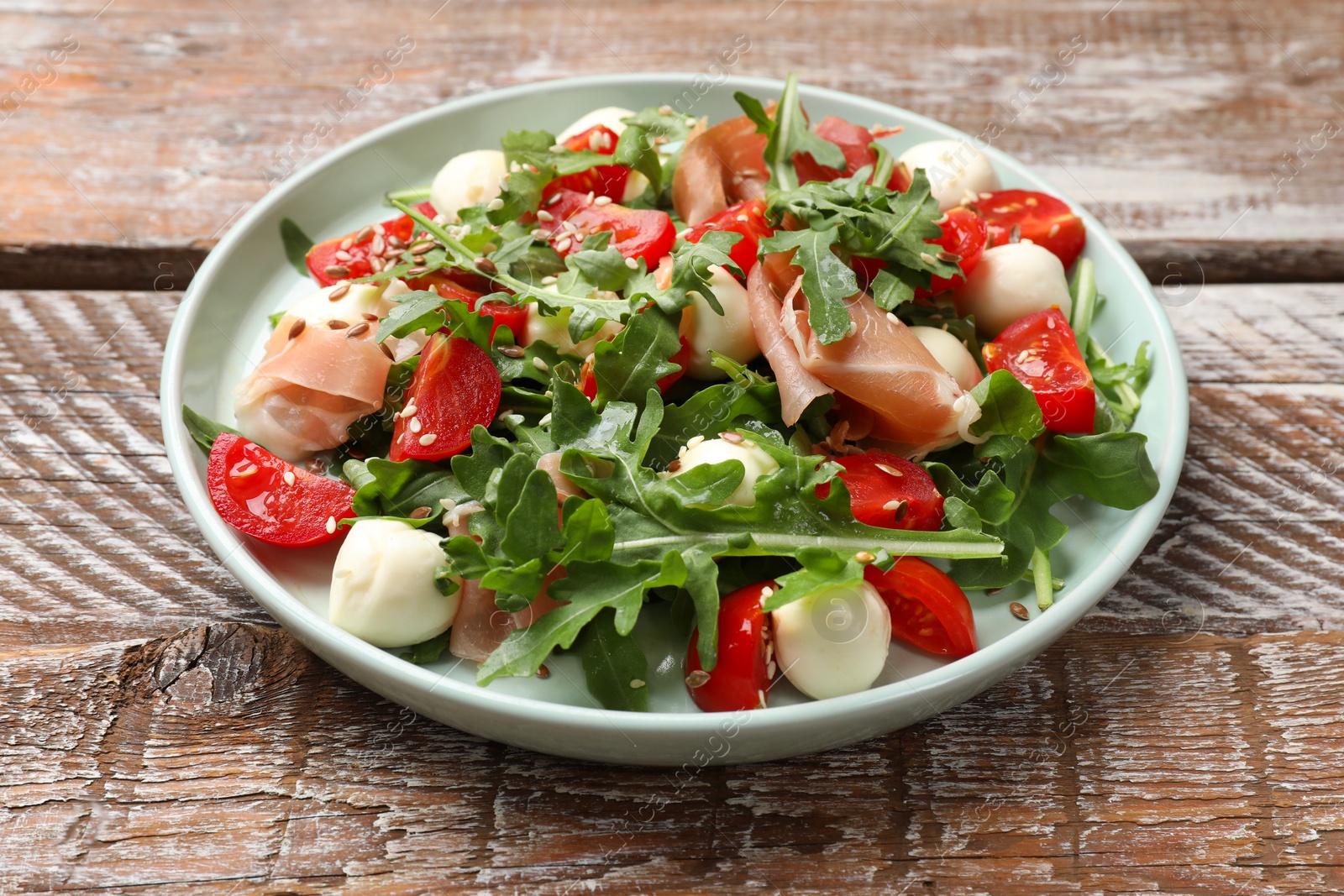 Photo of Tasty salad with arugula, mozzarella cheese, tomatoes and jamon on wooden table, closeup