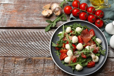 Photo of Tasty salad with arugula, mozzarella cheese, tomatoes and jamon on wooden table, flat lay. Space for text