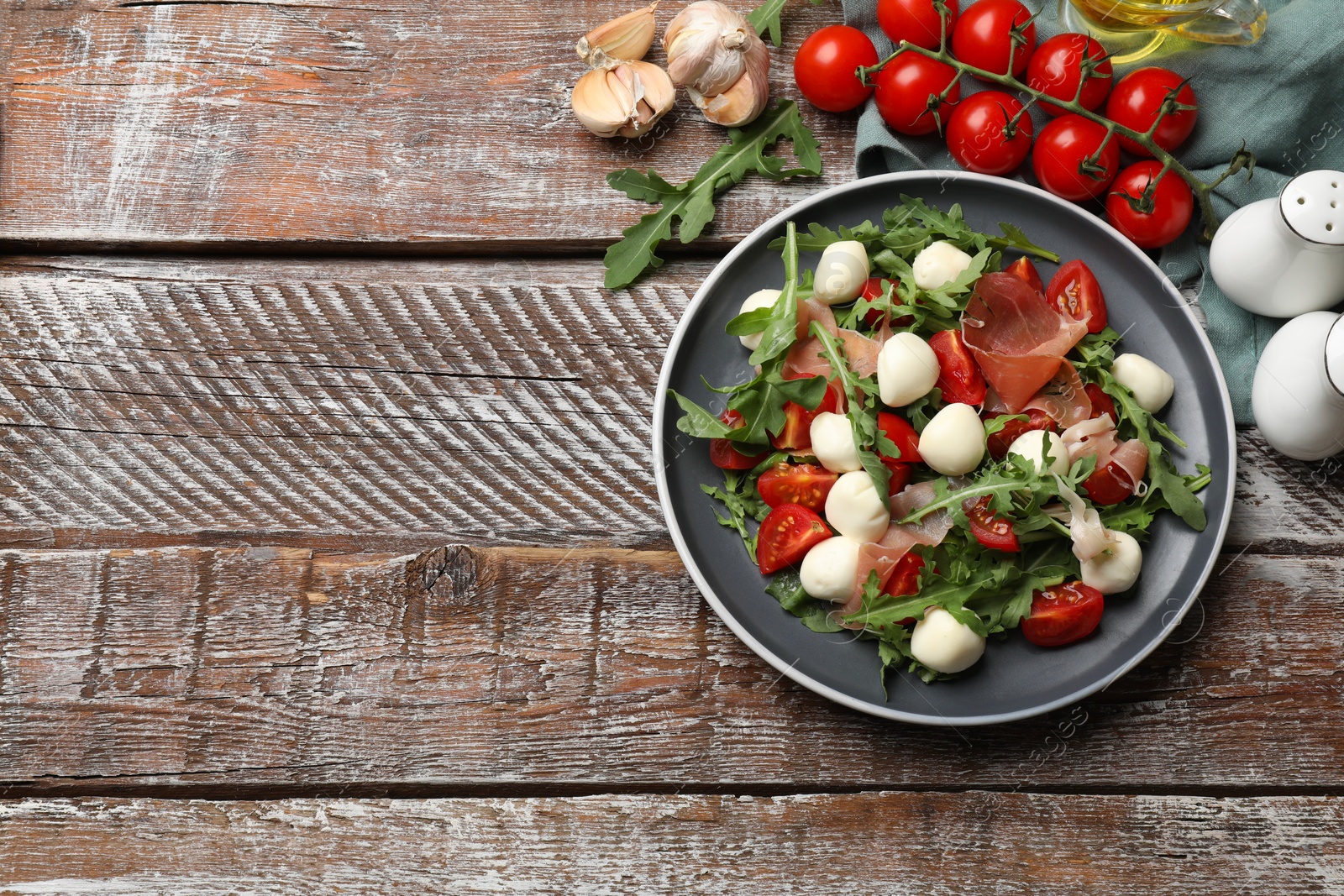 Photo of Tasty salad with arugula, mozzarella cheese, tomatoes and jamon on wooden table, flat lay. Space for text