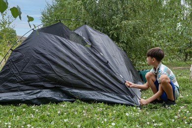 Photo of Little boy setting up camping tent outdoors