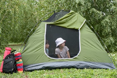 Photo of Girl and her brother resting in camping tent on green grass outdoors