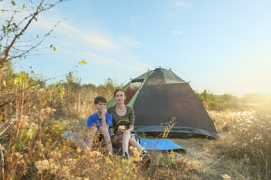 Photo of Mother and son eating apples near camping tent