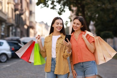 Happy women with colorful shopping bags using smartphone outdoors