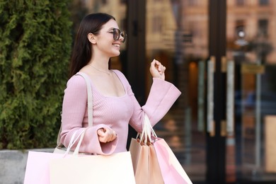 Happy woman with colorful shopping bags outdoors, space for text