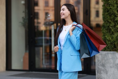 Happy woman with colorful shopping bags outdoors, space for text