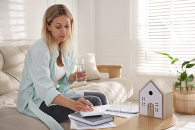 Budget planning. Woman with glass of water using calculator at table indoors