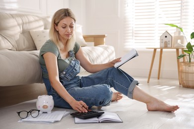 Budget planning. Woman with notebook using calculator on floor indoors