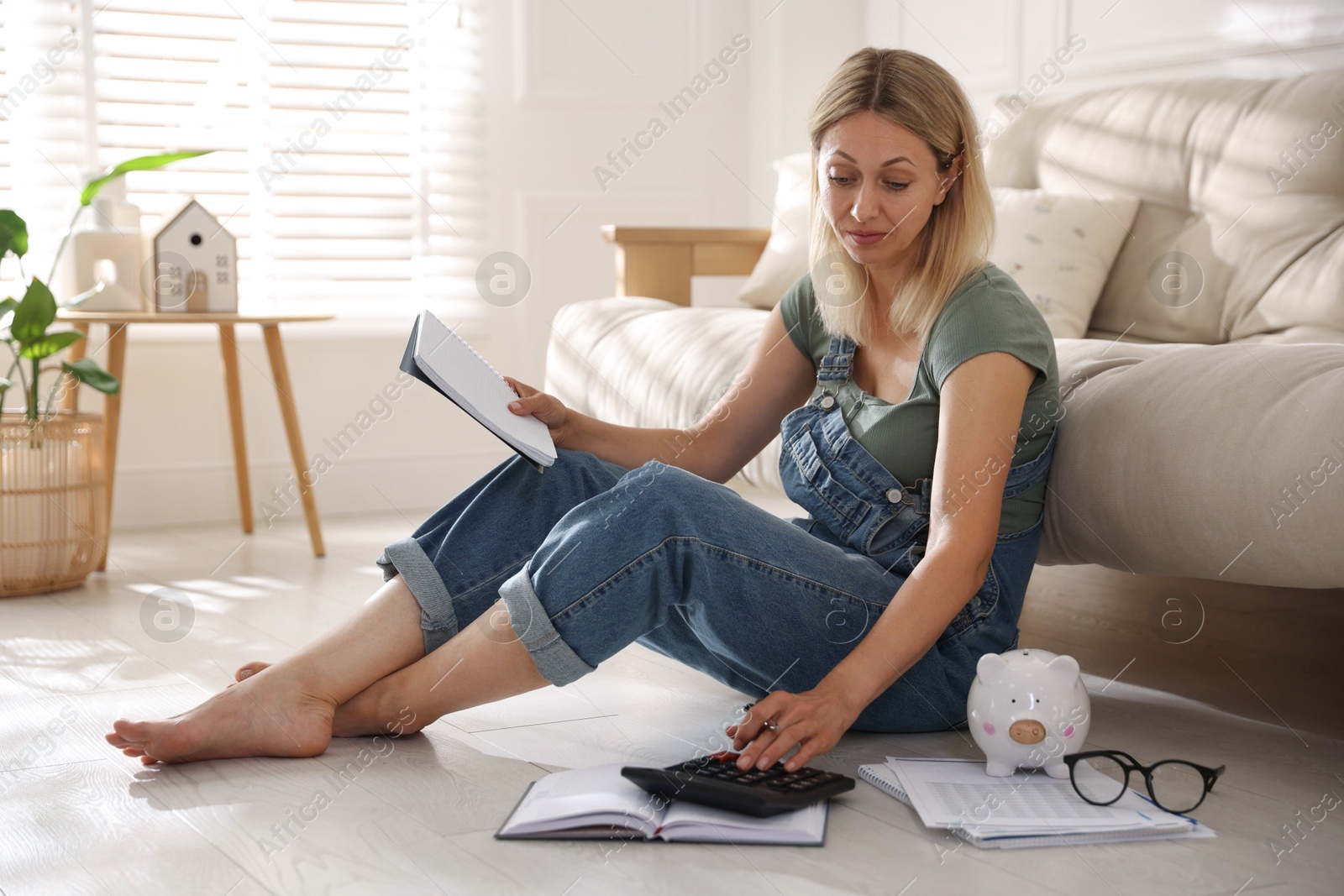 Photo of Budget planning. Woman with notebook using calculator on floor indoors