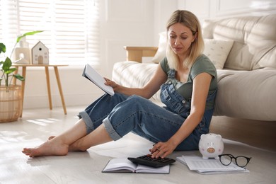 Photo of Budget planning. Woman with notebook using calculator on floor indoors