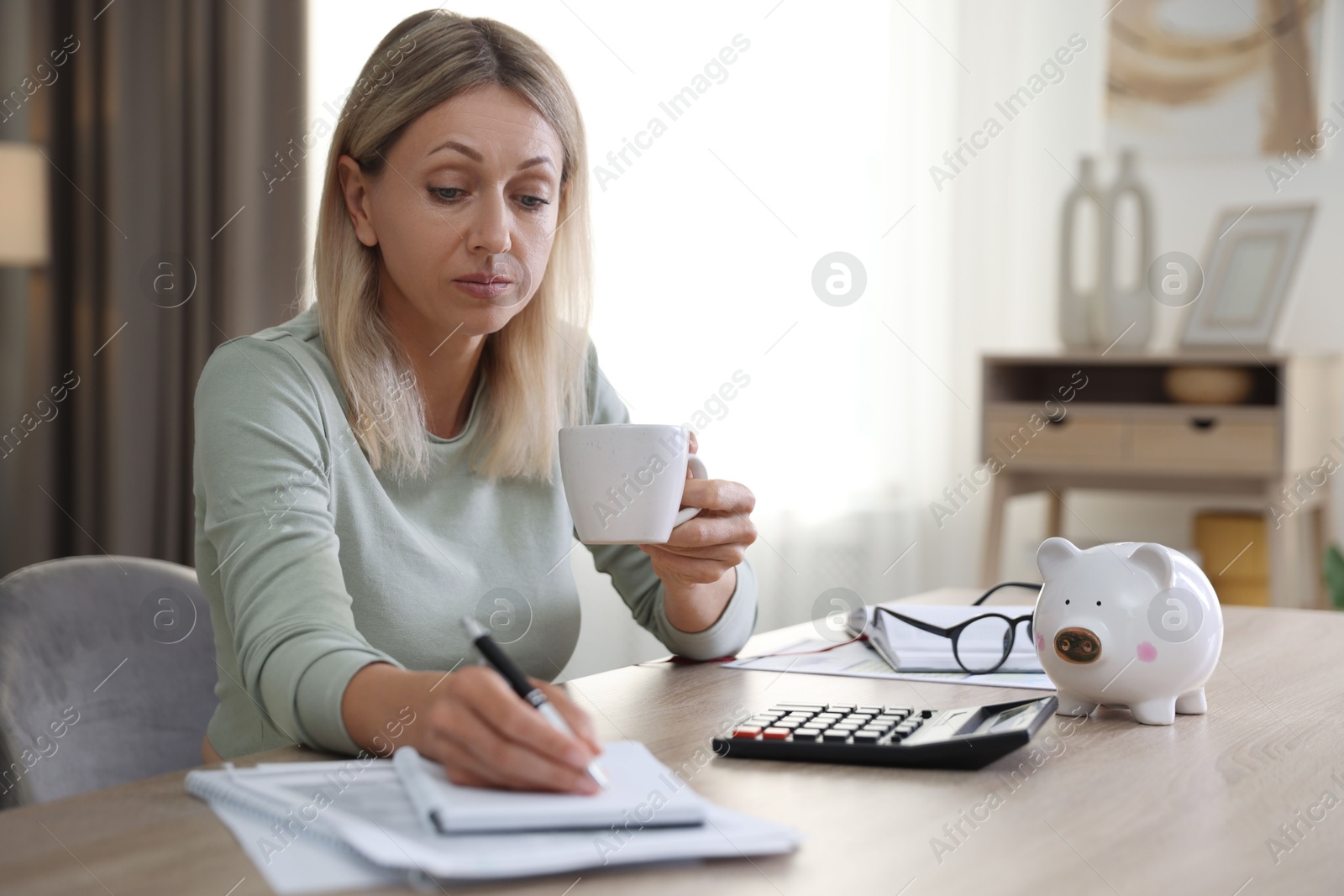 Photo of Budget planning. Woman with cup of drink taking notes at table indoors