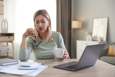 Budget planning. Woman with glasses and cup of drink at table indoors