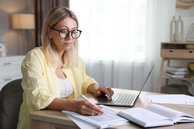 Budget planning. Woman using laptop while working with accounting documents at table indoors