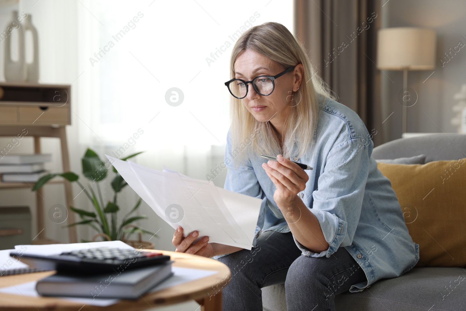 Photo of Budget planning. Woman working with accounting documents on sofa indoors