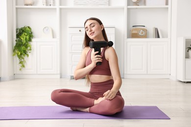 Photo of Woman using percussive massager to relieve trapezius muscle on mat at home