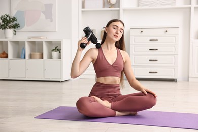 Woman using percussive massager to relieve trapezius muscle on mat at home