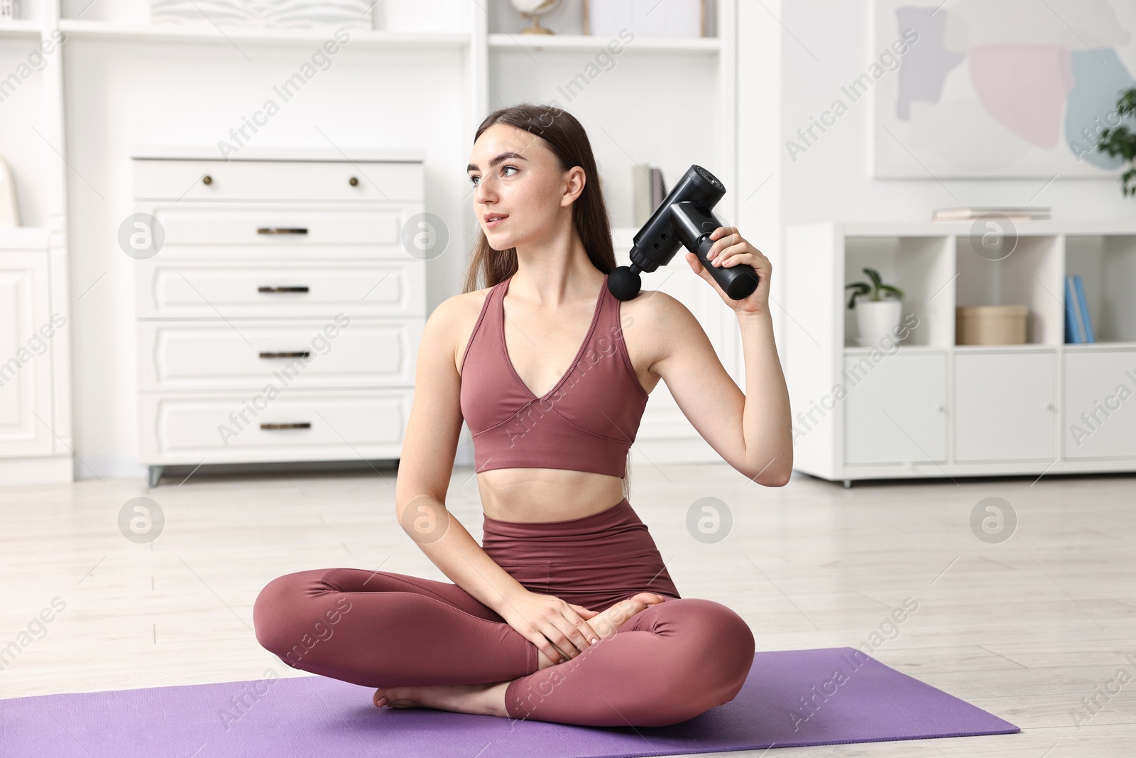 Photo of Woman using percussive massager to relieve trapezius muscle on mat at home