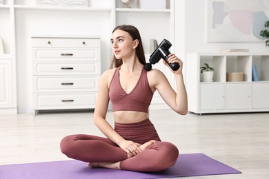 Photo of Woman using percussive massager to relieve trapezius muscle on mat at home