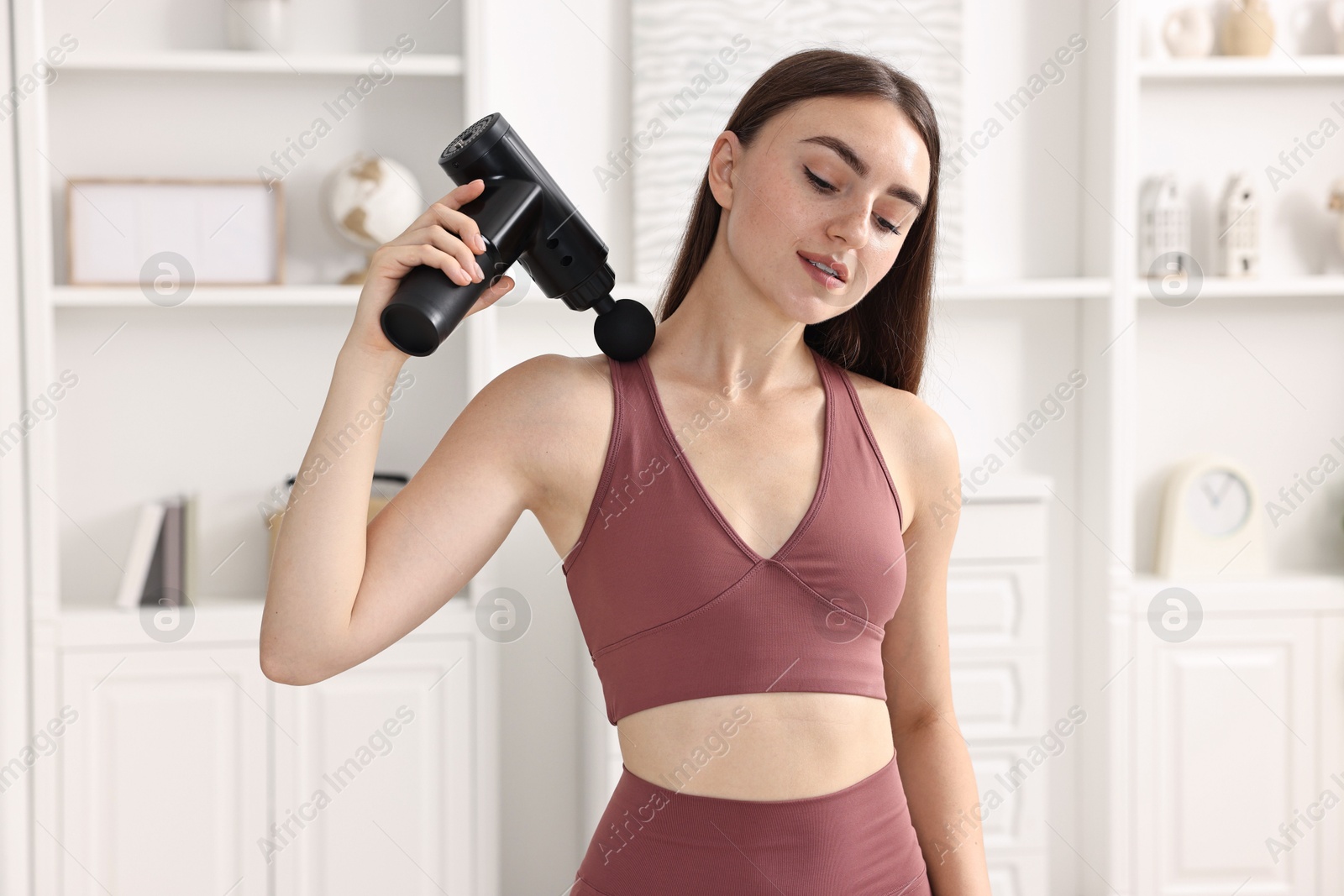 Photo of Woman using percussive massager to relieve trapezius muscle at home