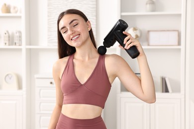 Woman using percussive massager to relieve trapezius muscle at home