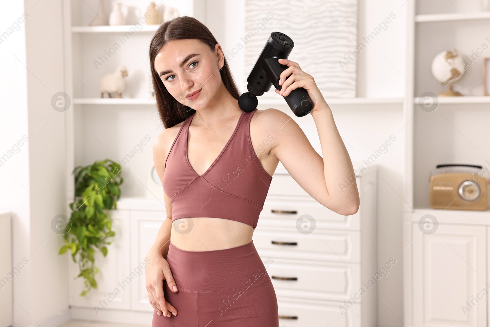 Photo of Woman using percussive massager to relieve trapezius muscle at home