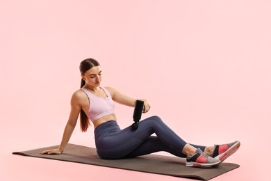 Woman using percussive massager to relax hip muscles on mat against pink background