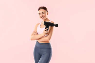 Young woman with percussive massager on pink background