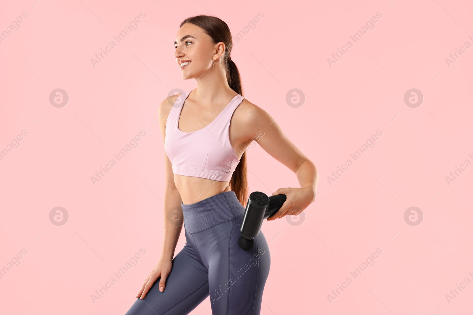 Photo of Woman using percussive massager to relax hip muscles on pink background