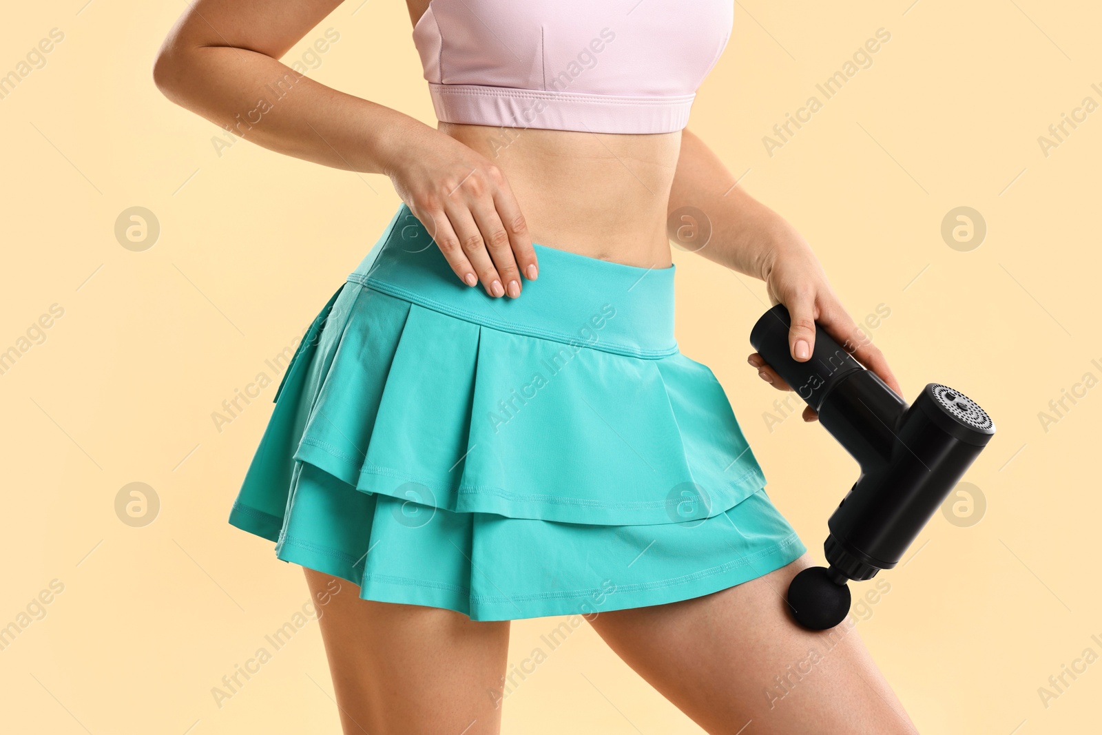 Photo of Woman using percussive massager to relax thigh muscles on beige background, closeup