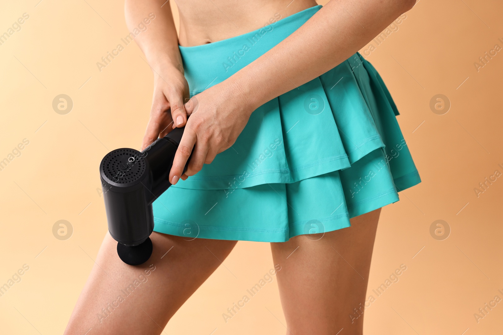 Photo of Woman using percussive massager to relax thigh muscles on beige background, closeup