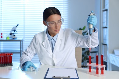 Photo of Laboratory testing. Doctor dripping blood sample into test tube at table indoors