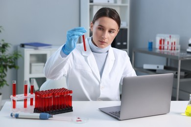 Laboratory testing. Doctor holding test tube with blood sample at table indoors