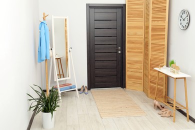 Clothing rack, mirror, houseplant and stylish furniture in hallway