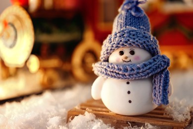 Photo of Cute decorative snowman on artificial snow against blurred background, closeup