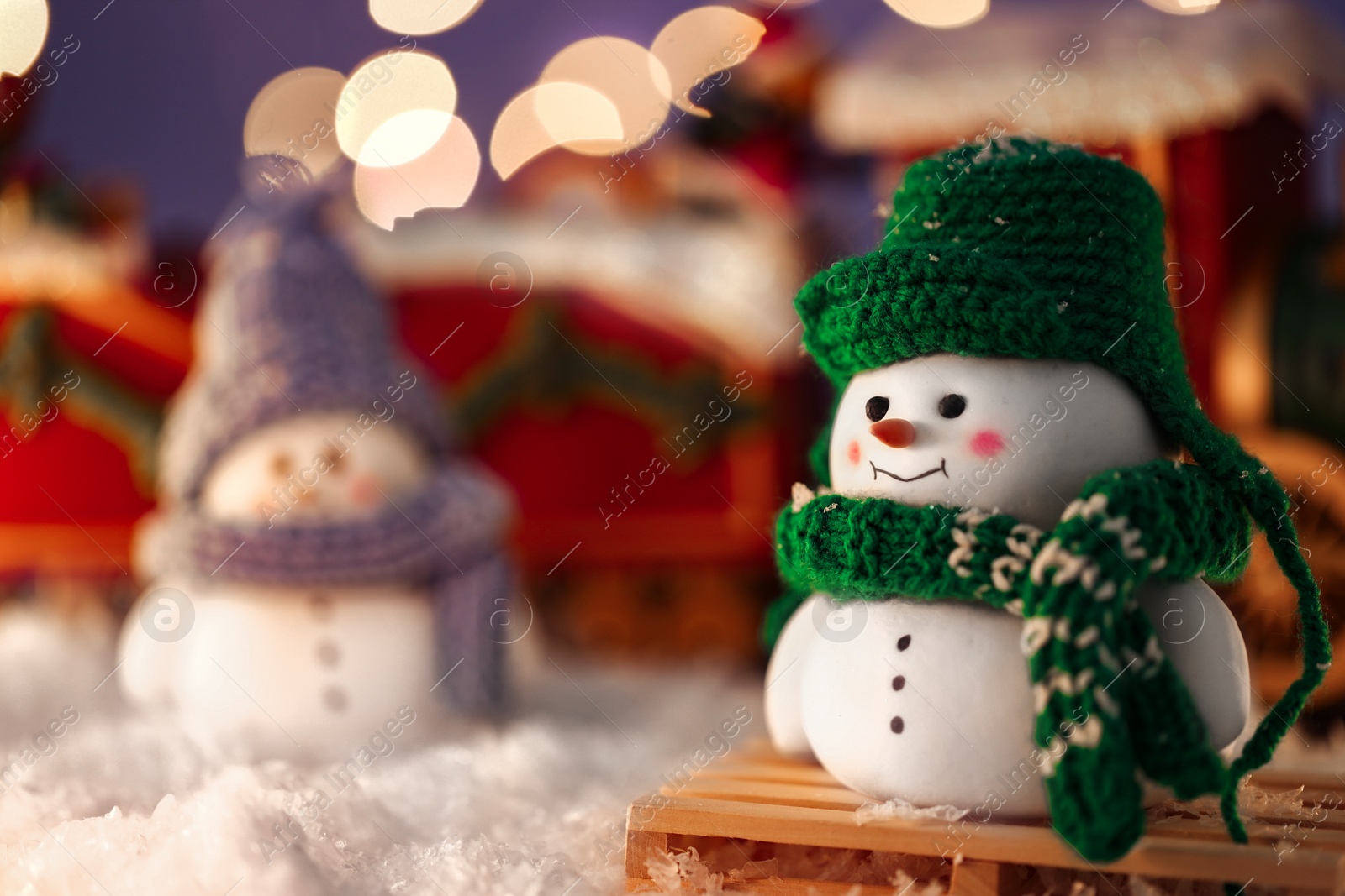 Photo of Cute decorative snowmen on artificial snow against blurred lights, selective focus