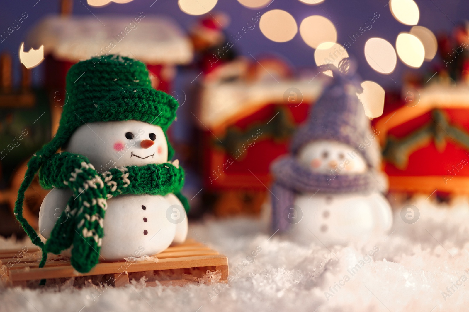 Photo of Cute decorative snowmen on artificial snow against blurred lights, selective focus