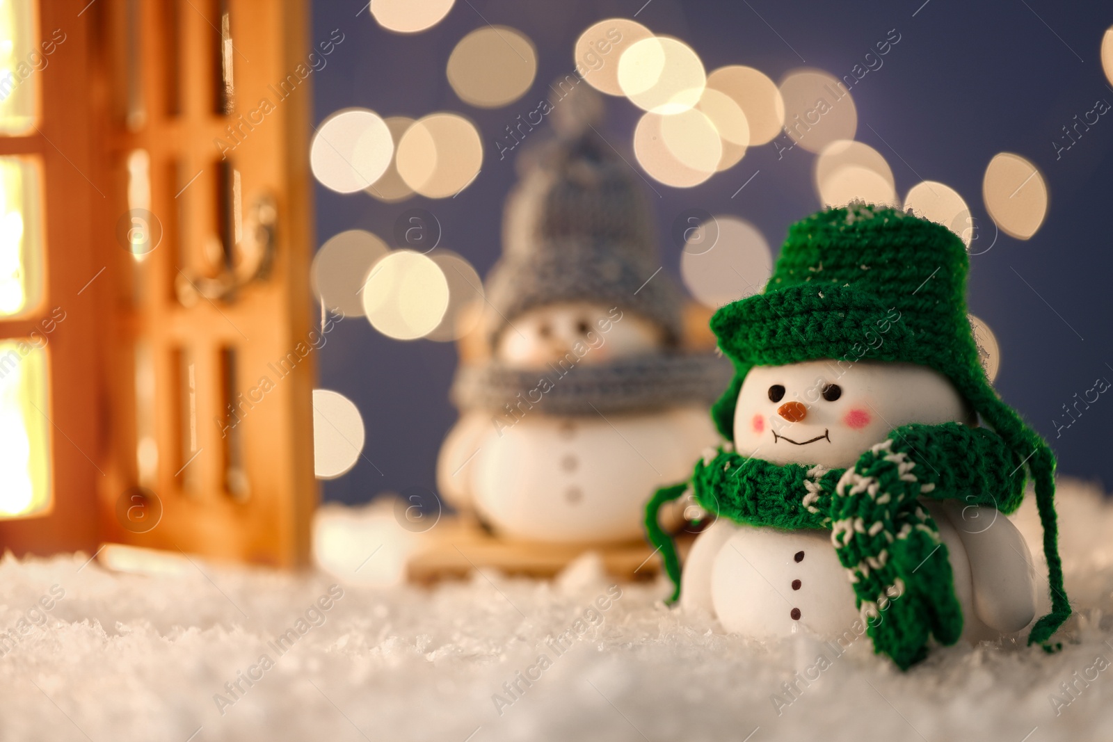 Photo of Cute decorative snowmen and lantern on artificial snow against blurred lights, selective focus