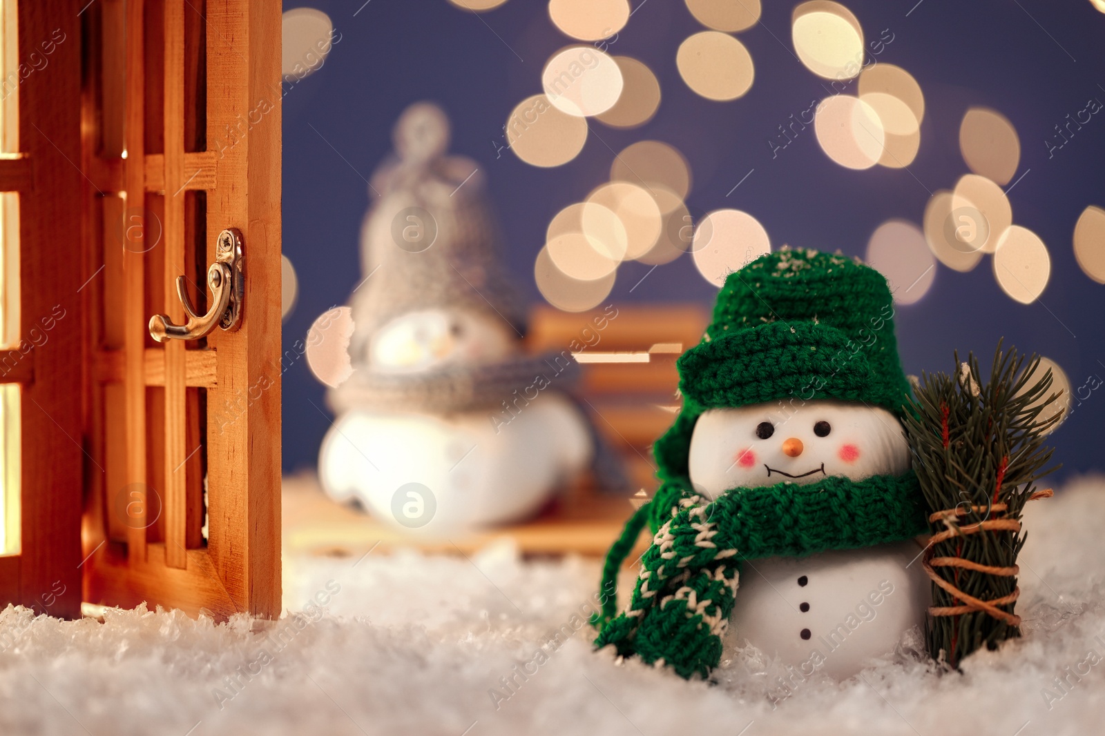 Photo of Cute decorative snowmen, fir tree branches and lantern on artificial snow against blurred lights, selective focus