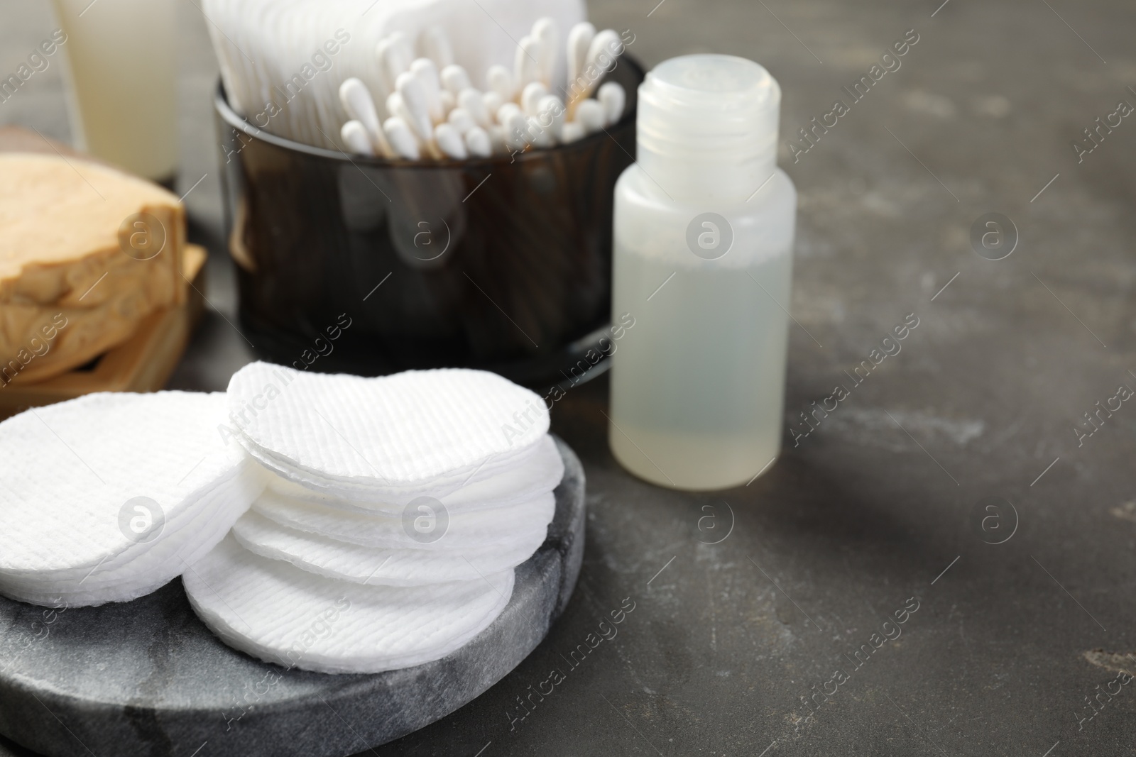 Photo of Many cotton pads and other toiletries on grey textured table, closeup