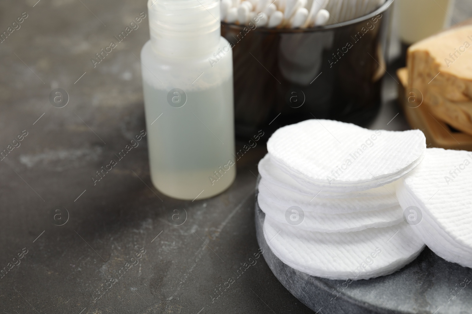 Photo of Many cotton pads and other toiletries on grey textured table, closeup