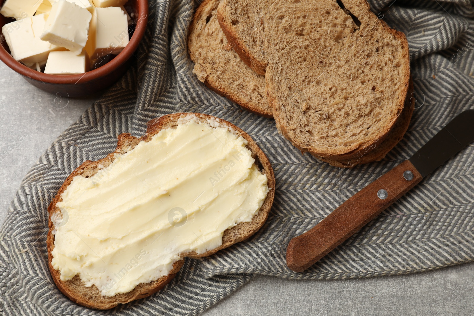 Photo of Fresh bread with butter and knife on grey table, flat lay