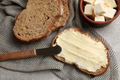 Photo of Fresh bread with butter and knife on grey table, flat lay