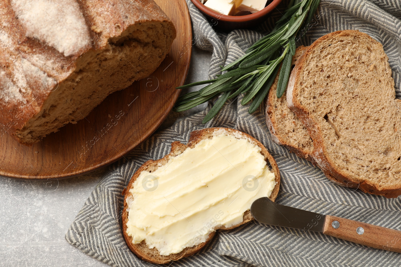 Photo of Fresh bread with butter and knife on grey table, flat lay