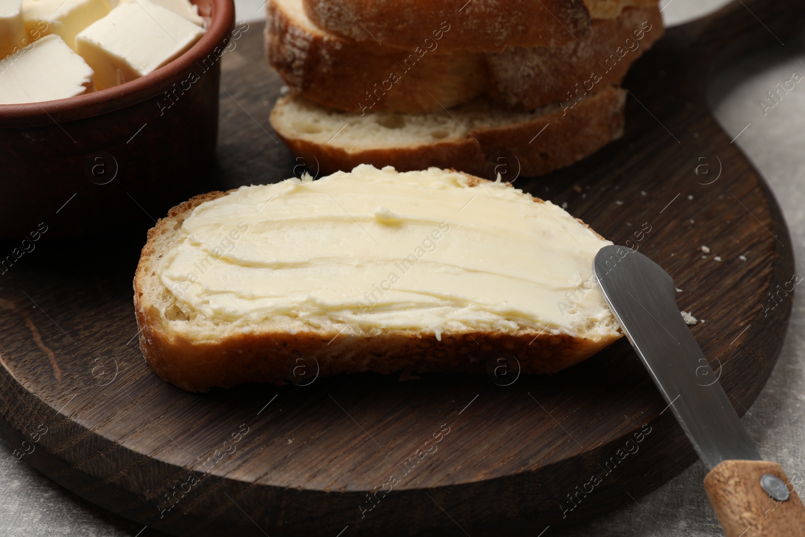 Photo of Fresh bread with butter and knife on grey table, closeup