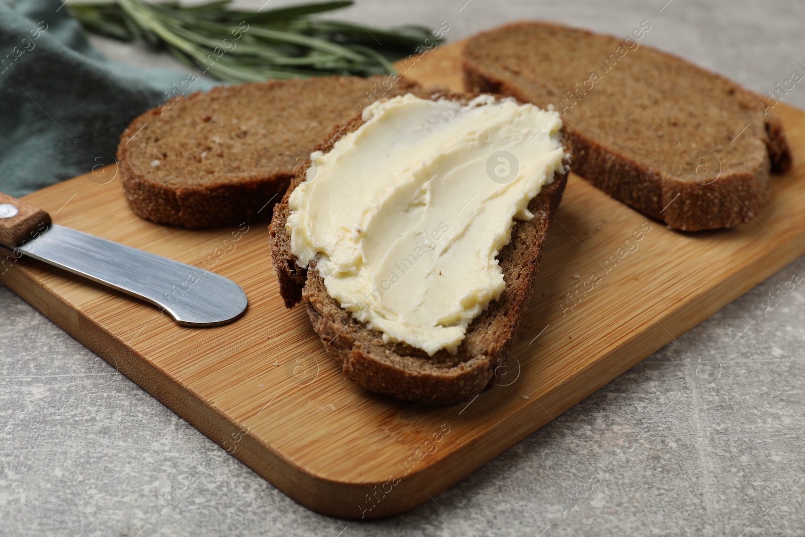 Photo of Fresh bread with butter and knife on grey table, closeup