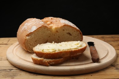 Photo of Fresh bread with butter and knife on wooden table, closeup