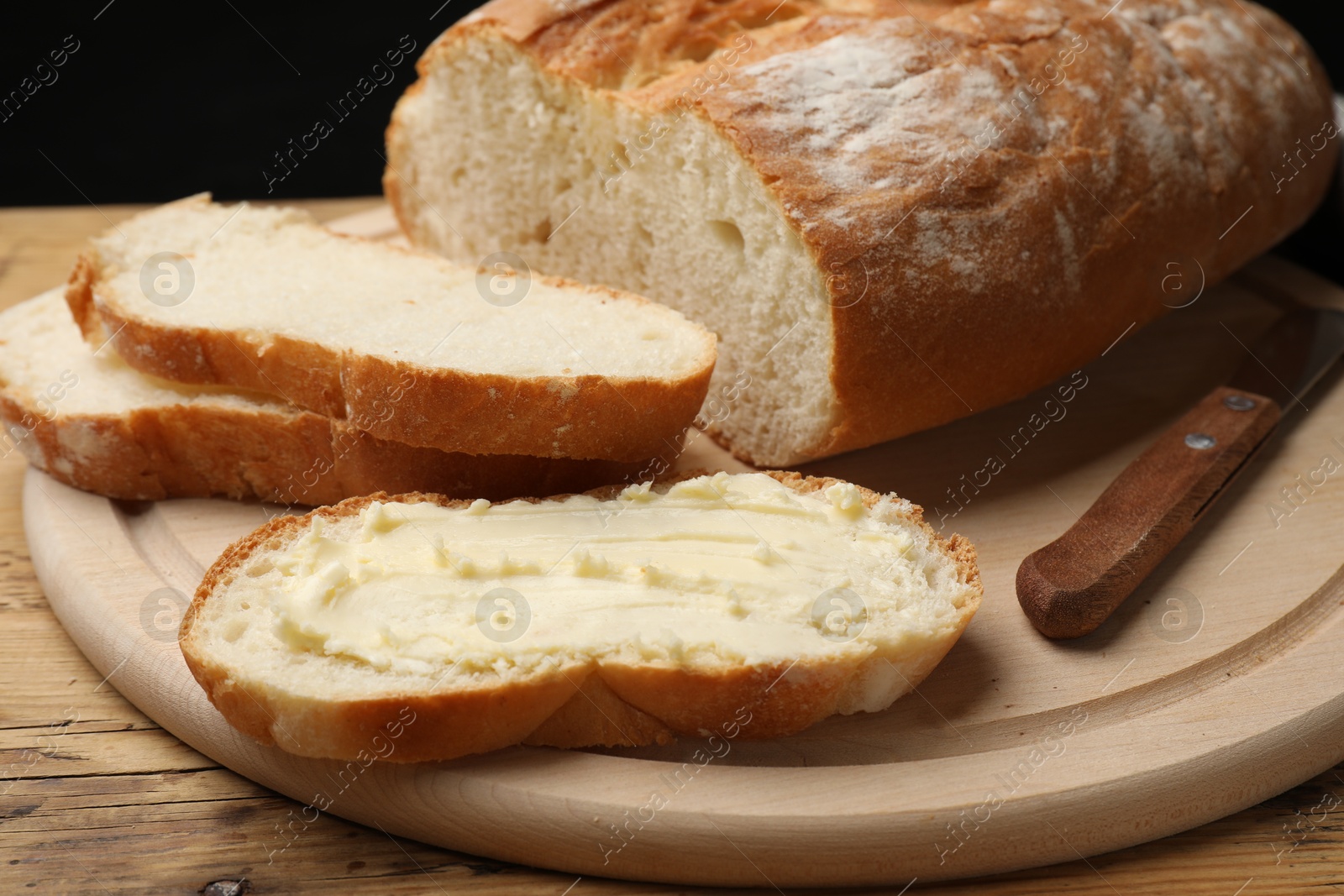 Photo of Fresh bread with butter and knife on wooden table, closeup