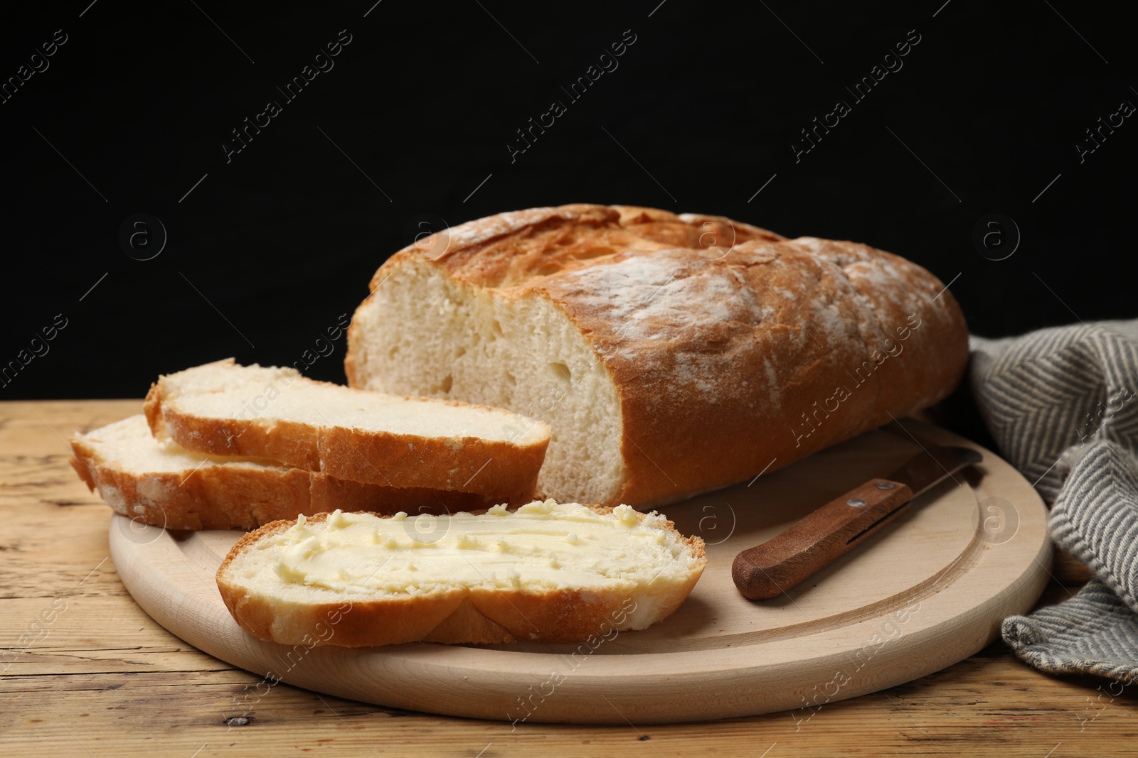 Photo of Fresh bread with butter and knife on wooden table, closeup