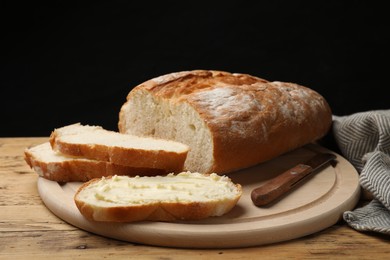 Photo of Fresh bread with butter and knife on wooden table, closeup