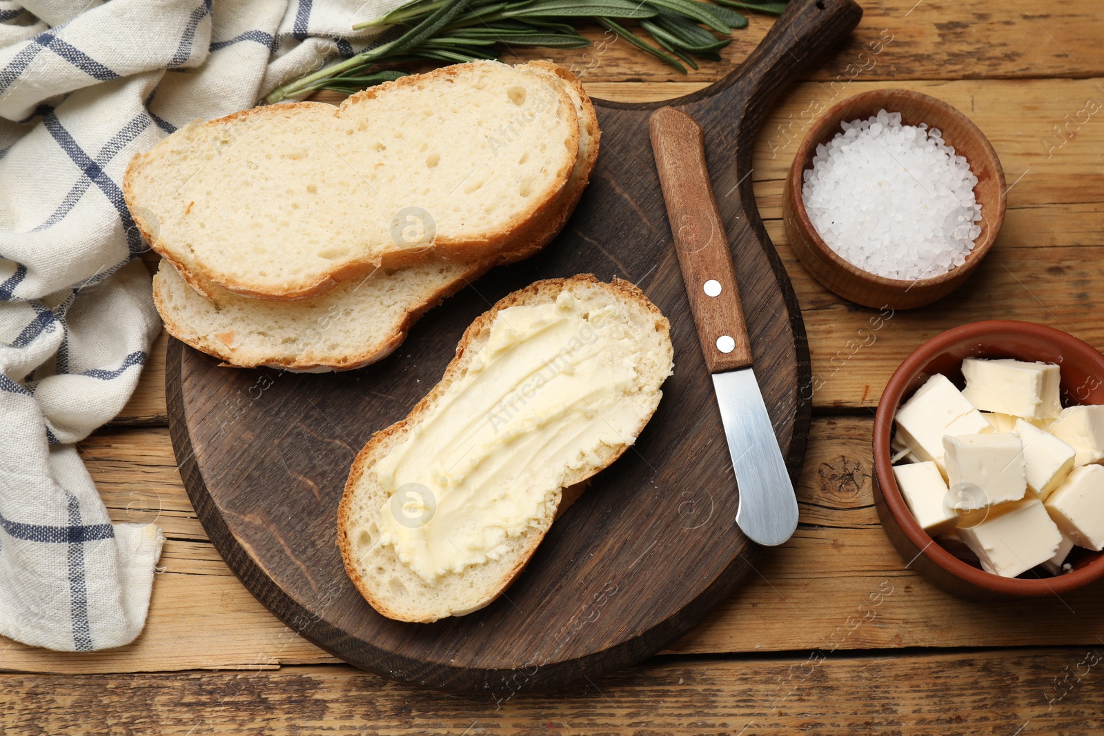 Photo of Fresh bread with butter and knife on wooden table, flat lay